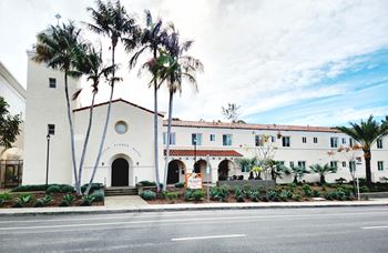 A white building with a red roof and palm trees in front.